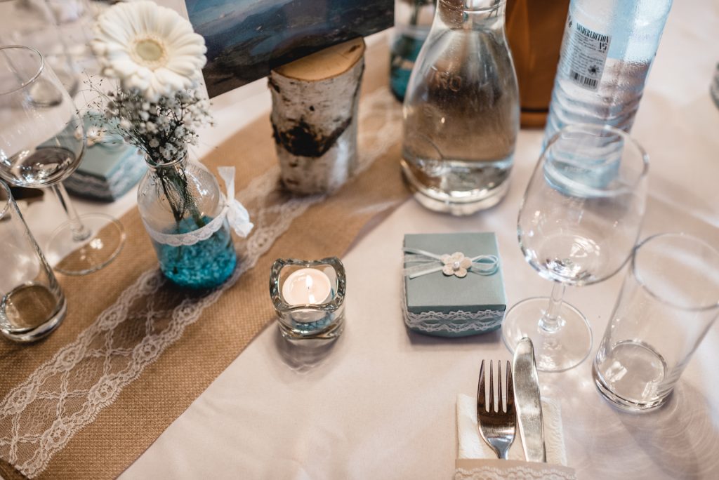 Gastgeschenk mit Schleife neben Kerze, weißer Blume und festlichem Gedeck